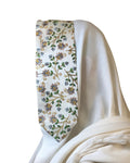 Couronne Fleuri Or présentée sur un tissu blanc, avec bordure florale et détails dorés