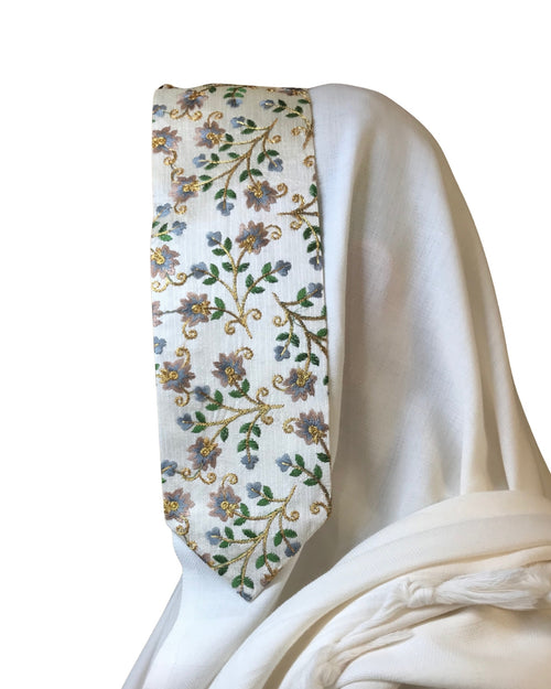 Couronne Fleuri Or présentée sur un tissu blanc, avec bordure florale et détails dorés